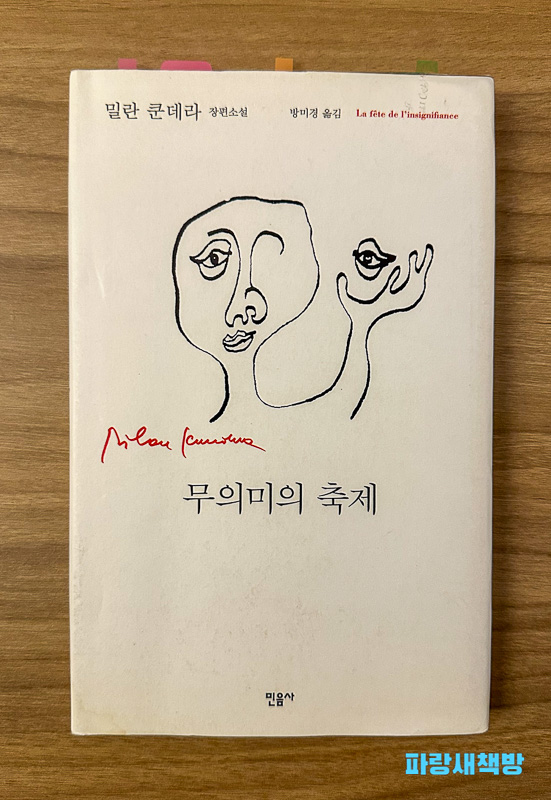 밀란 쿤데라의 소설 『무의미의 축제』 한국어판 표지. 미니멀한 흑백 선 그림과 작가의 서명이 붉은색으로 인쇄되어 있다.